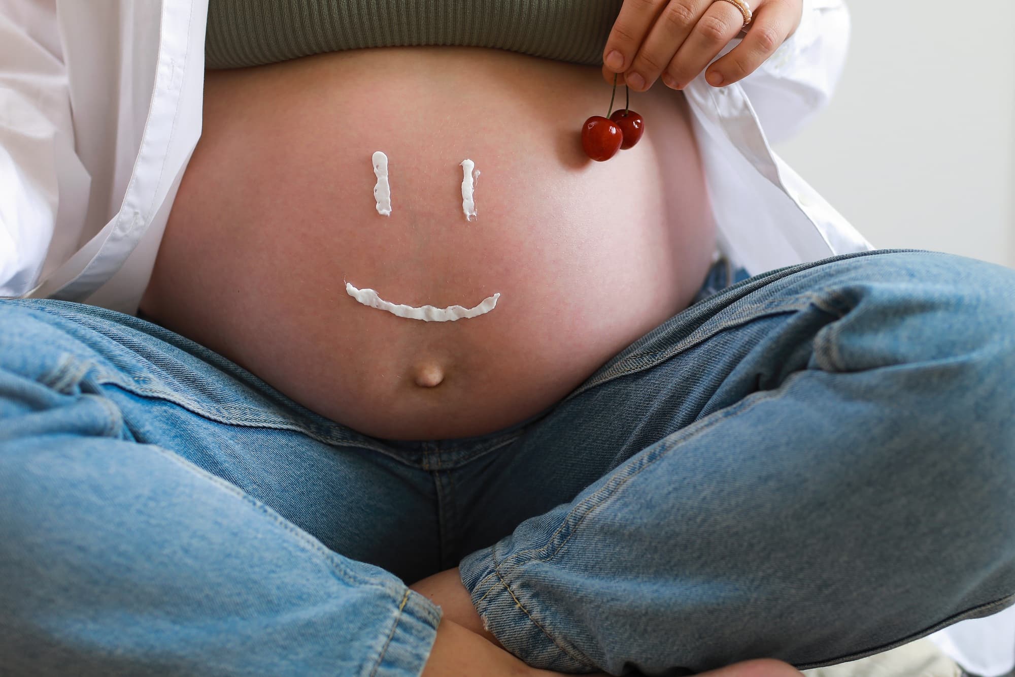 Close-up of torso of young pregnant model applying moisturizer on her belly to avoid stretch marks.