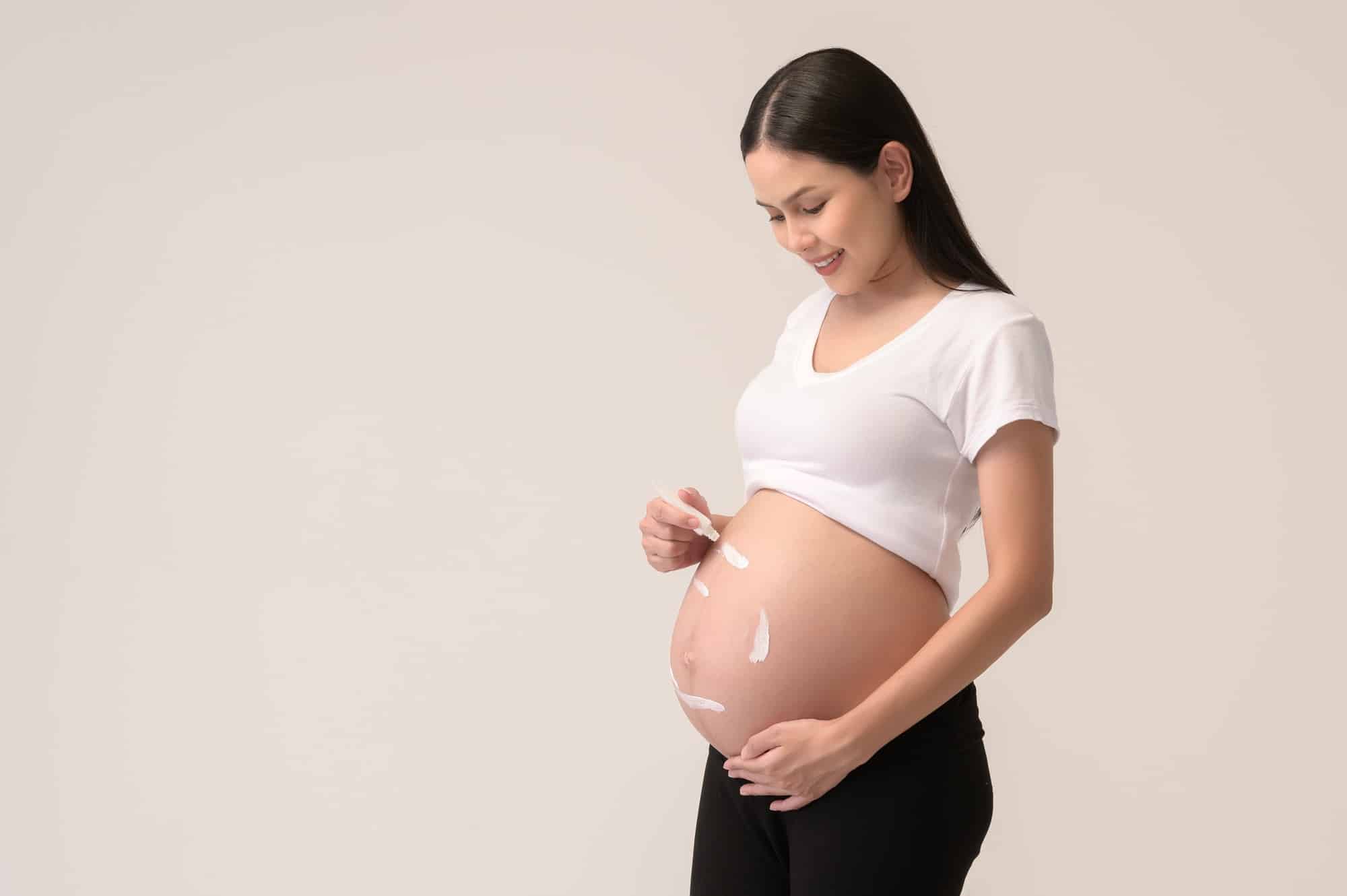 pregnant woman applying moisturizing, stretch mark cream on belly