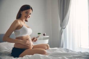 Woman lubricating and moisturizing pregnant belly with cream for stretch mark