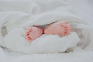 barefooted baby covering white blanket
